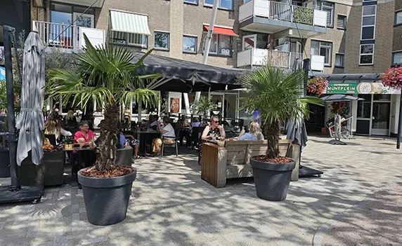 Gasten op het terras van Eetcafé de Vuurtoren tussen de palmbomen op het Muntplein