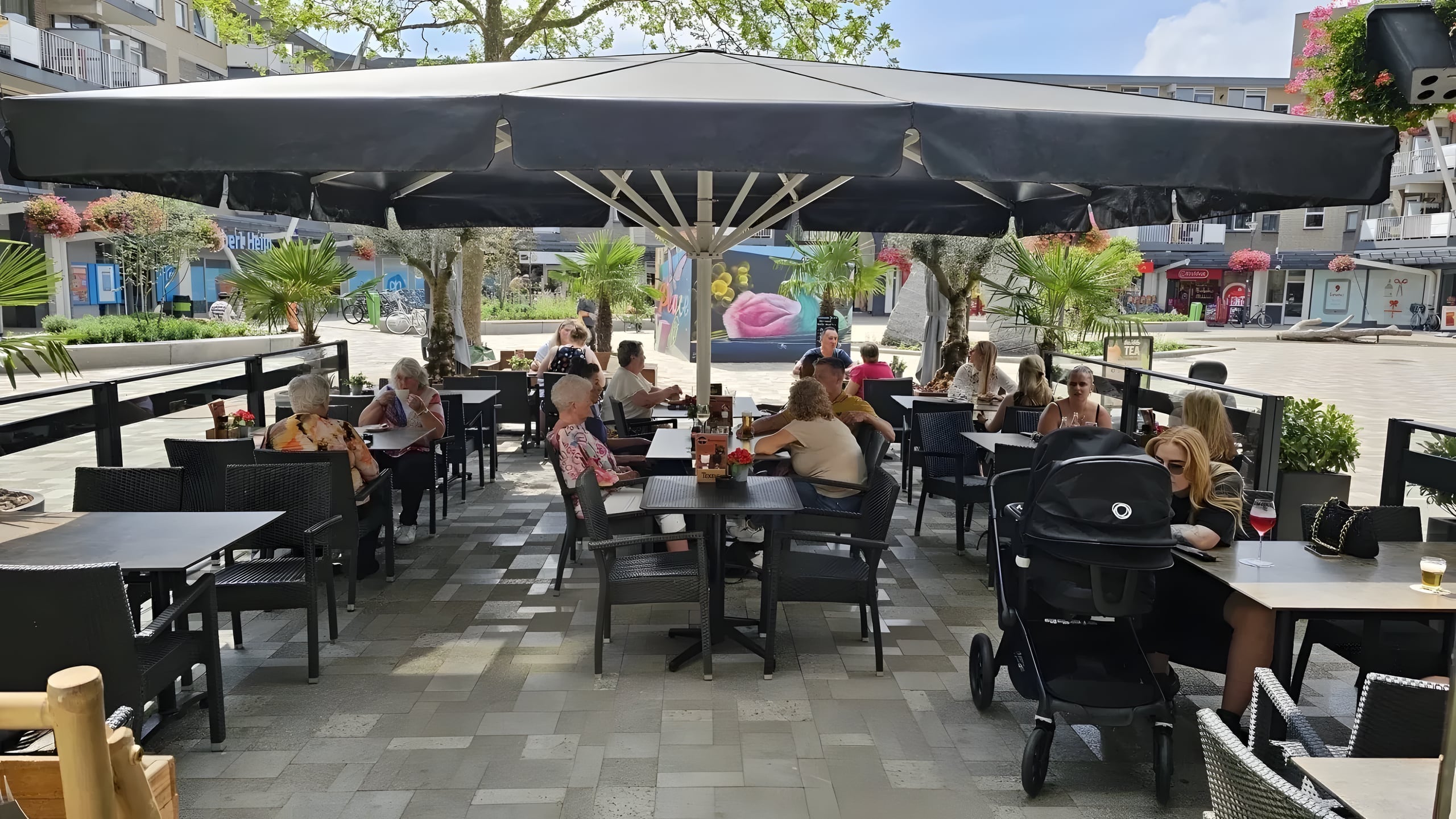 Zonnig terras van Eetcafé de Vuurtoren onder een groot zwart parasol, vol gasten aan het Muntplein in Nieuwegein